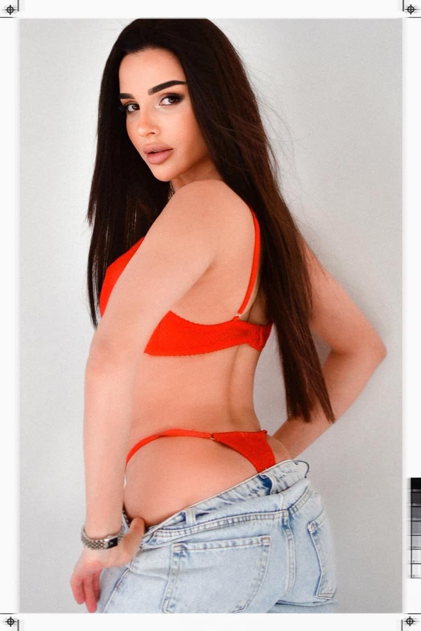 Profile view of a woman in a red bikini top and thong, with denim jeans pulled down to her upper thighs.